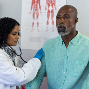 Biracial female doctor using stethoscope and examinating african american male patient. Hospital, medicine and healthcare.